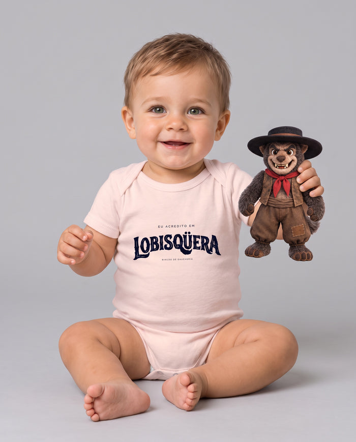 Bebê sentado e sorrindo com o Body Eu Acredito em Lobisqüera na cor rosa bebê, segurando um boneco do lobisomem de chapéu e lenço vermelho
