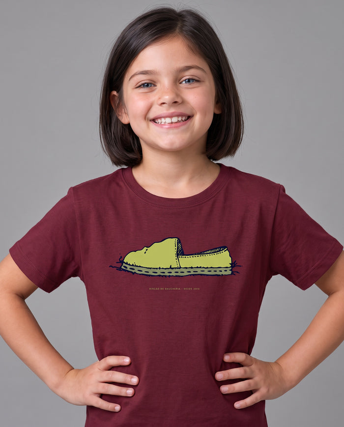 Menina sorrindo com a Camiseta Alpargata Identidade de Campo infantil, na cor bordeaux, com a estampa da alpargata no peito