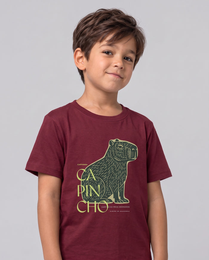 Menino sorrindo, vestindo a camiseta infantil Capincho na cor bordeaux, com a estampa da capivara