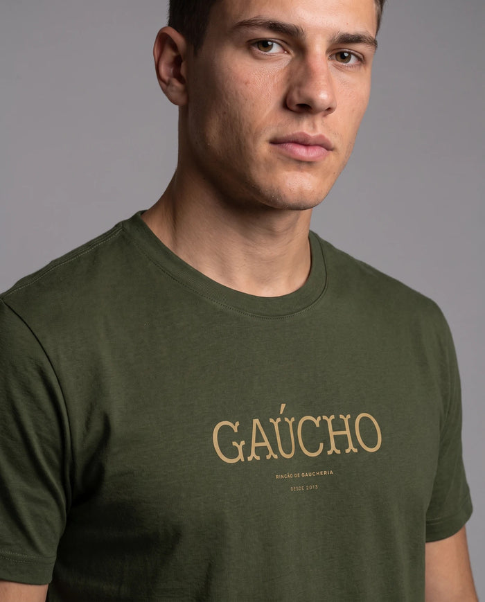 Homem vestindo a camiseta Gaúcho em algodão peruano na cor verde musgo, com detalhe da estampa tipográfica dourada da palavra Gaúcho no peito