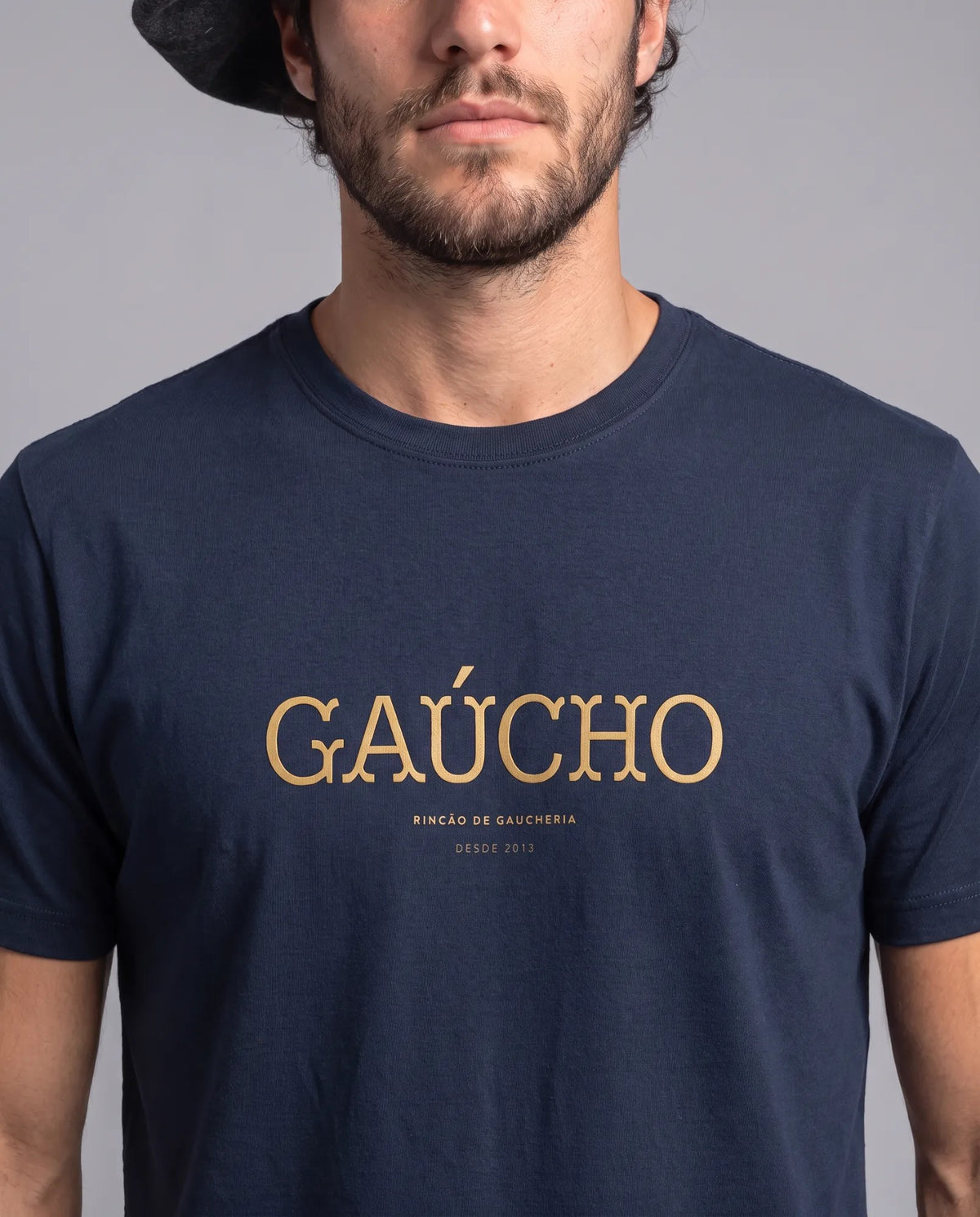 Detalhe da camiseta Gaúcho da Gaucheria, modelagem masculina, na cor azul marinho, com estampa tipográfica dourada da palavra Gaúcho no peito