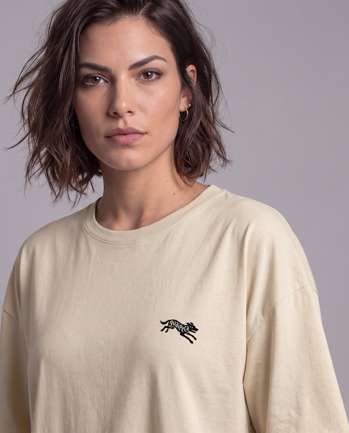 Mulher vestindo a Camiseta Guaipeca da Série Sem Alarde, modelagem oversized unissex, na cor areia