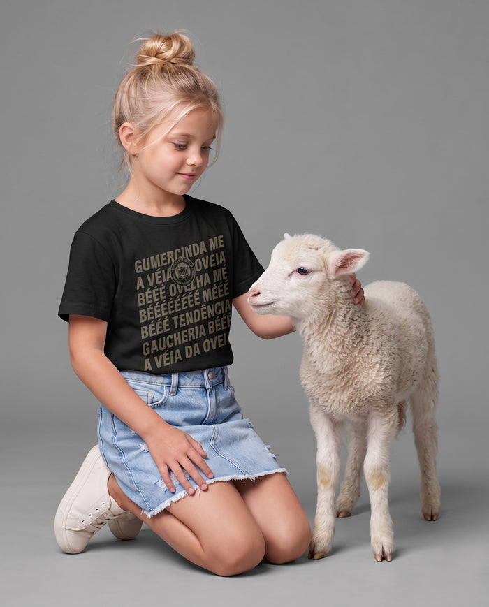 Menina ajoelhada ao lado de um cordeiro, vestindo a camiseta infantil Ovelha é Tendência na cor preta