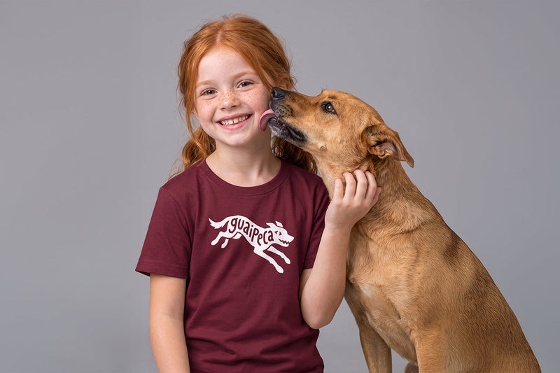 Menina usando camiseta infantil Guaipeca ao lado de um cachorro caramelo