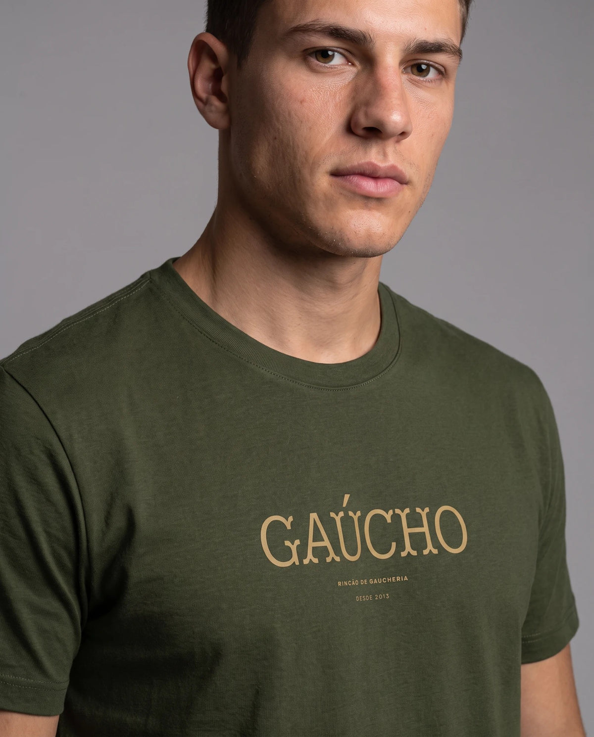 Homem vestindo a camiseta Gaúcho em algodão peruano na cor verde musgo, com detalhe da estampa tipográfica dourada da palavra Gaúcho no peito