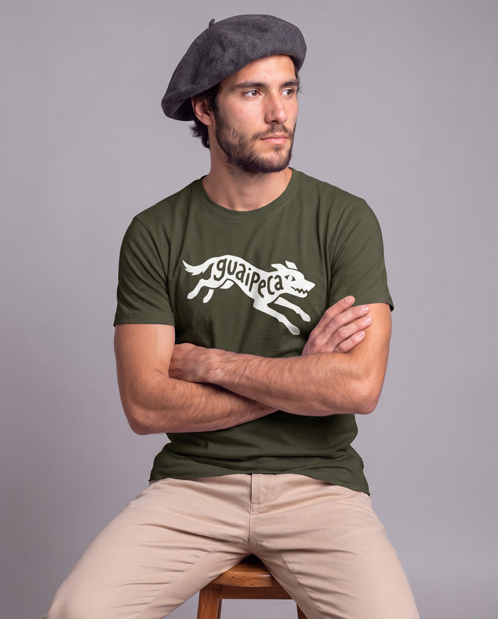 Homem de boina sentado de braços cruzados vestindo a Camiseta Guaipeca da linha Marca de Fala em algodão peruano, modelagem masculina, na cor verde musgo