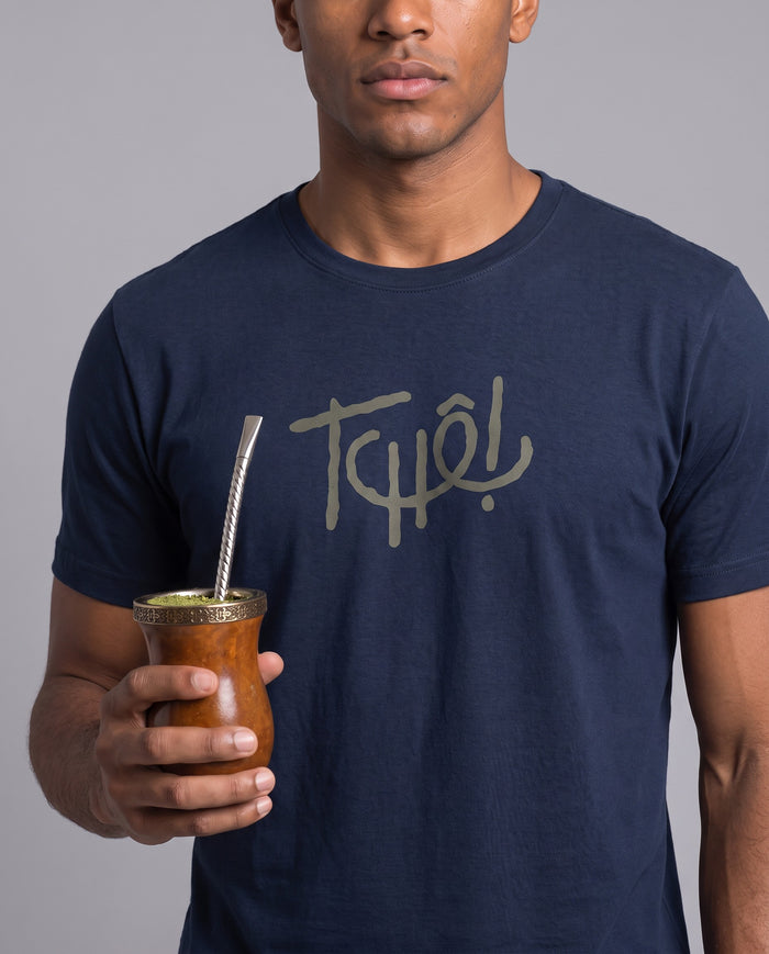 Homem com uma cuia de chimarrão vestindo a camiseta Tchê! Clássico em algodão peruano, modelagem masculina, na cor marinho