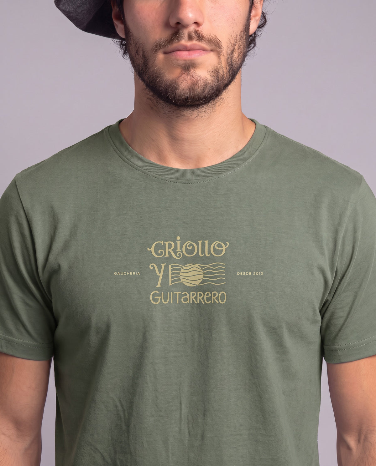 Detalhe da estampa Criollo y Guitarrero, em traço dourado, no peito da camiseta de algodão peruano verde oliva